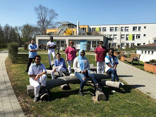 Auszubildende und junge Mitarbeitenden in der Pflege<span class='copy'>Stiftung Großheppacher Schwesternschaft</span> Auszubildende und junge Mitarbeitenden in der Pflege im Garten des Wilhelmine-Canz-Zentrums sitzen und stehen auf Baustämmen
